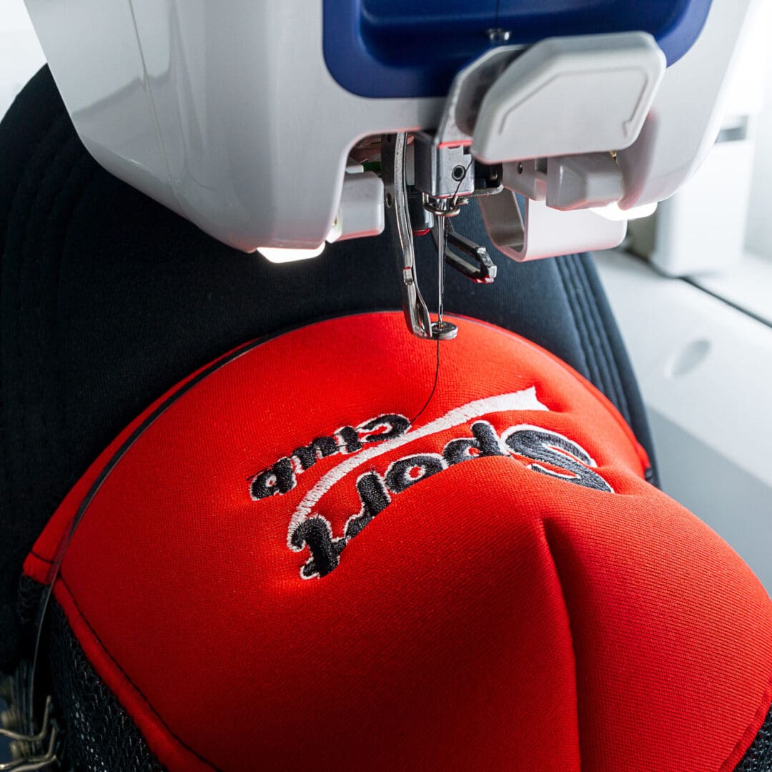 White Embroidery machine and red and black sport cap on the hoop, close up picture